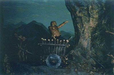 Cavewoman (his wife) pulls casually waving husband away in cart, now that he has discovered the wheel